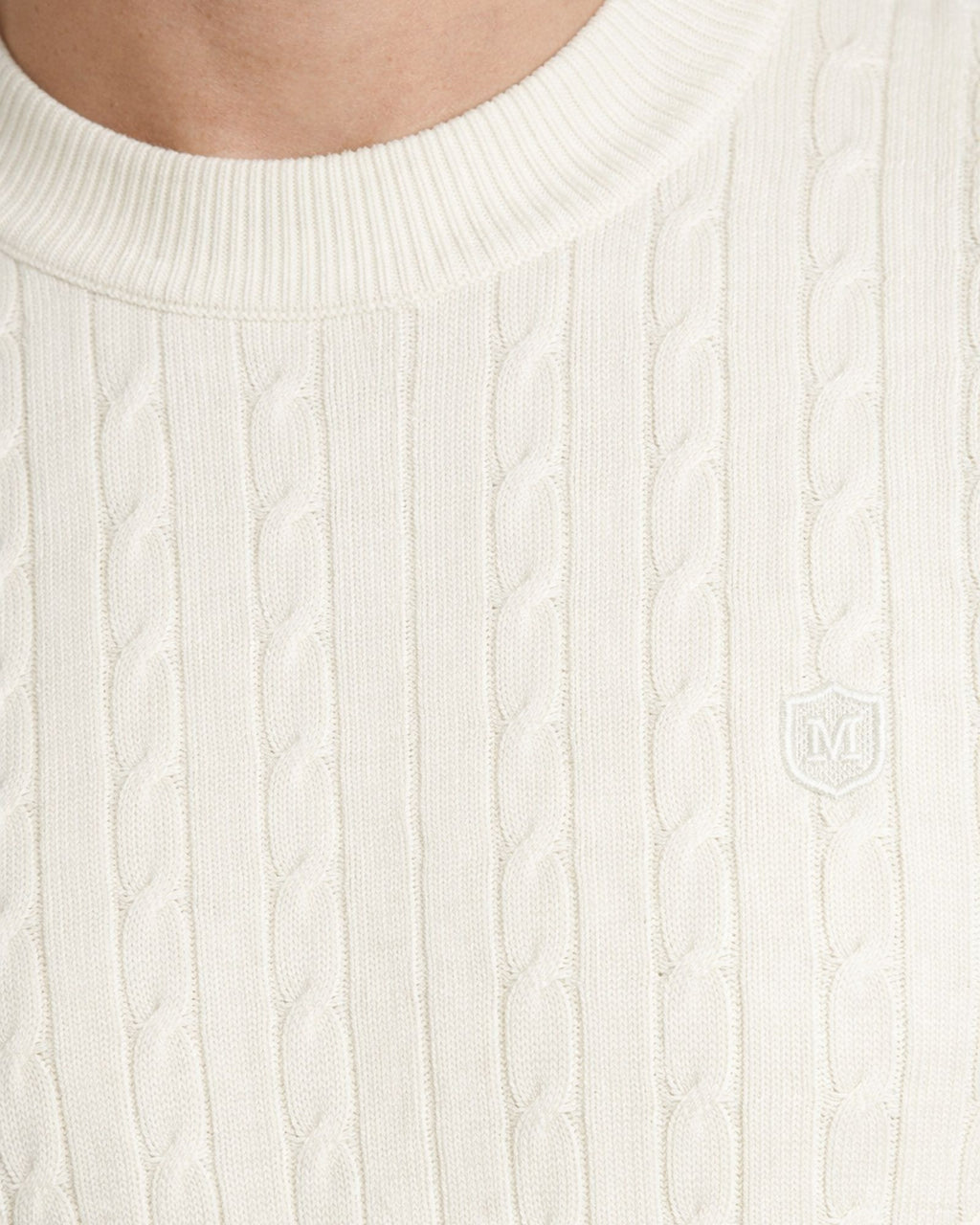 Detalle de suéter de punto color blanco con cuello caja y textura de trenzas, confeccionado en algodón premium para moda masculina de calidad.