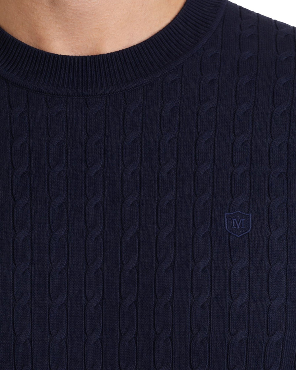 Detalle de suéter azul marino de punto con cuello caja en tejido 100% algodón, diseño de trenzas y logo bordado sutil, ideal para moda masculina premium.