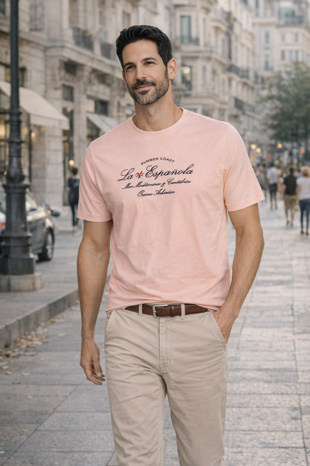 Hombre caminando por una calle urbana vistiendo una camiseta salmon de algodón y elastano con texto estampado, combinada con pantalones beige y cinturón marrón, moda masculina premium. la española, zaragoza