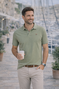 Hombre sonriente con polo verde pálido de algodón y elastano en entorno náutico, combinando estilo casual y comodidad, ideal para moda masculina premium.