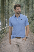 Hombre vestido con polo azul demil de algodón y elastano, modelo casual de moda masculina premium, posando en un entorno natural con árboles y sendero.