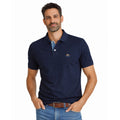 Hombre vistiendo polo azul marino de algodón con detalle bordado, estilo premium y corte clásico, combinado con cinturón marrón y jeans casuales.
