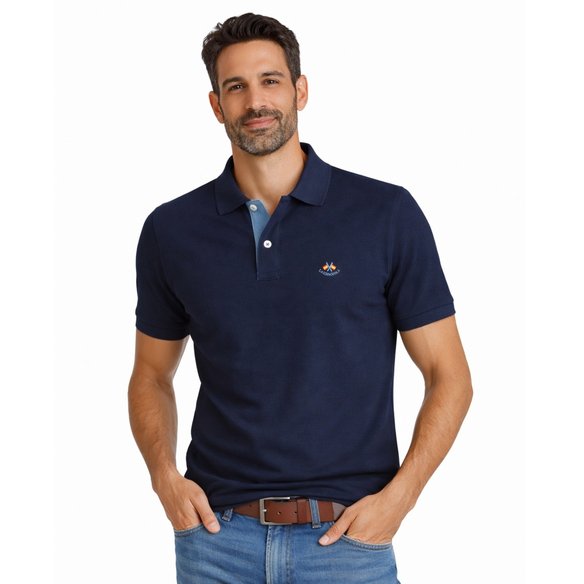 Hombre vistiendo polo azul marino de algodón con detalle bordado, estilo premium y corte clásico, combinado con cinturón marrón y jeans casuales.