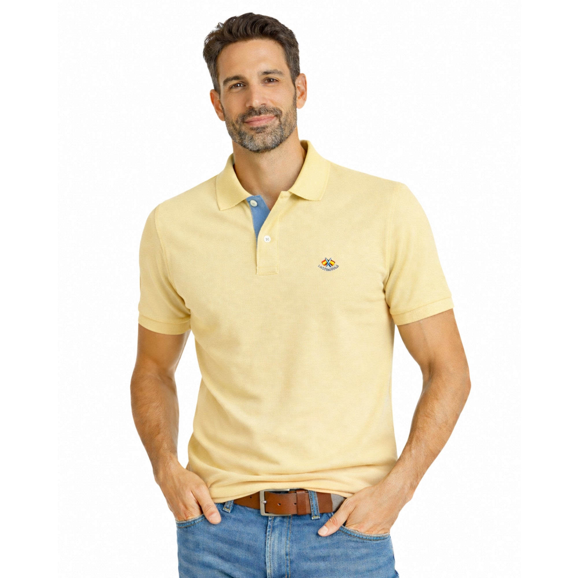 Hombre vistiendo polo amarillo coral de estilo premium con detalle bordado, combinado con jeans y cinturón marrón, moda masculina de alta calidad.